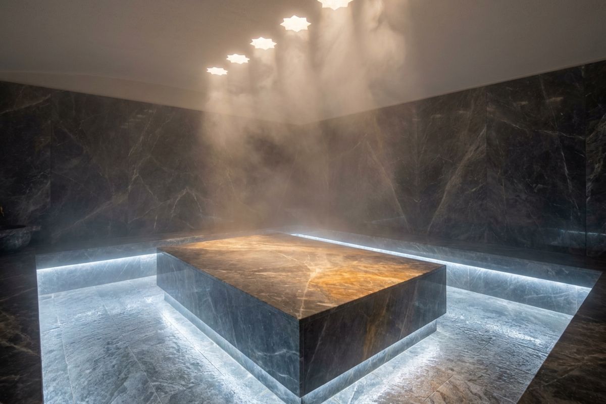 Hamam with a heated stone platform and steam under a dark marble ceiling
